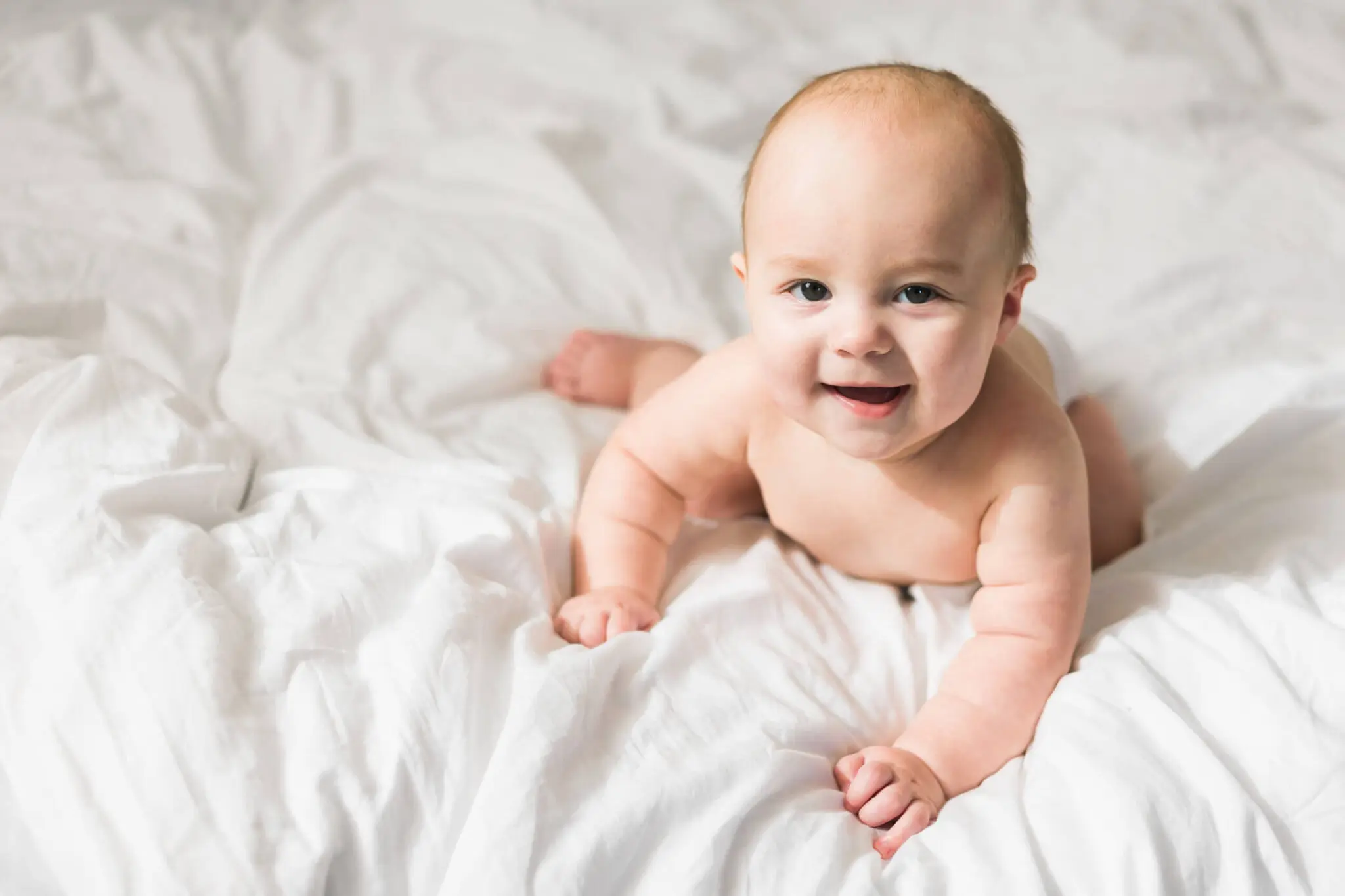 Smiling baby lying on white bed.