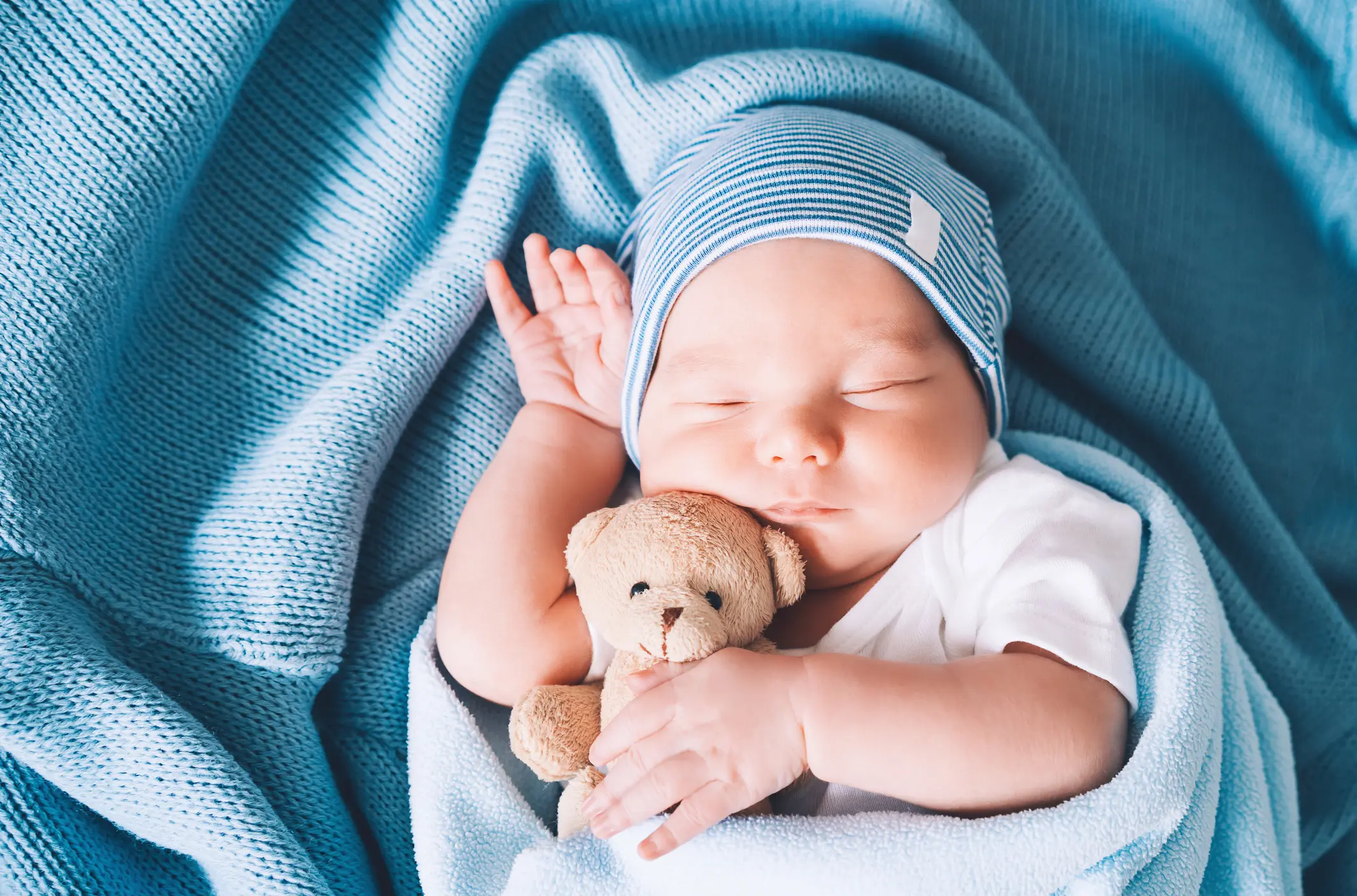 Newborn baby sleep at first days of life. Portrait of new born child boy one week old sleeping peacefully with a cute soft toy in crib in cloth background.